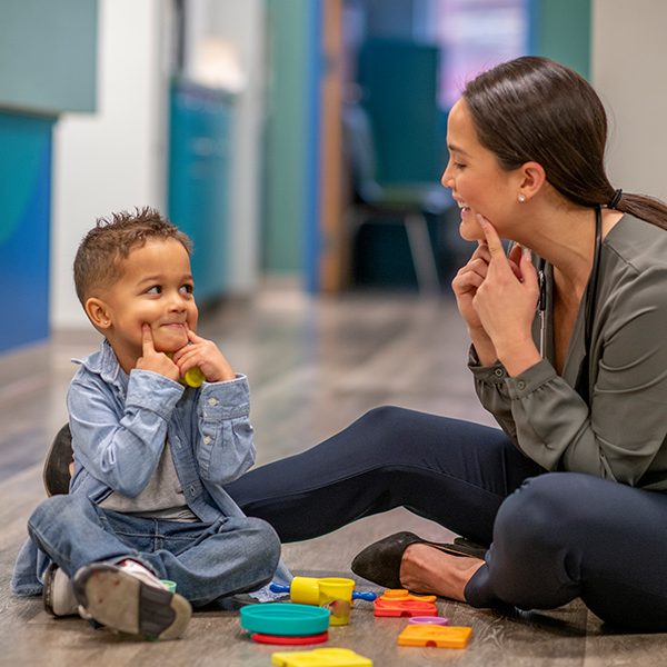 Toddler patient works with female provider using hands to make facial expressions.
