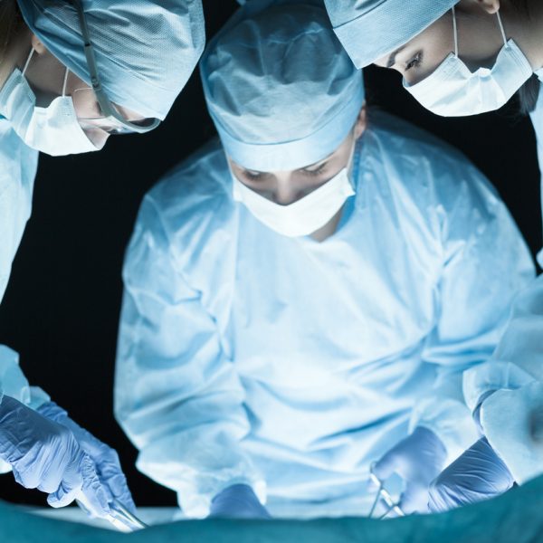 Medical team performing operation. Group of surgeon at work in operating theatre toned in blue